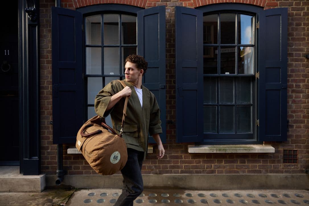 Tristan Alexander walking on a London street carrying a duffel bag, wearing olive jacket