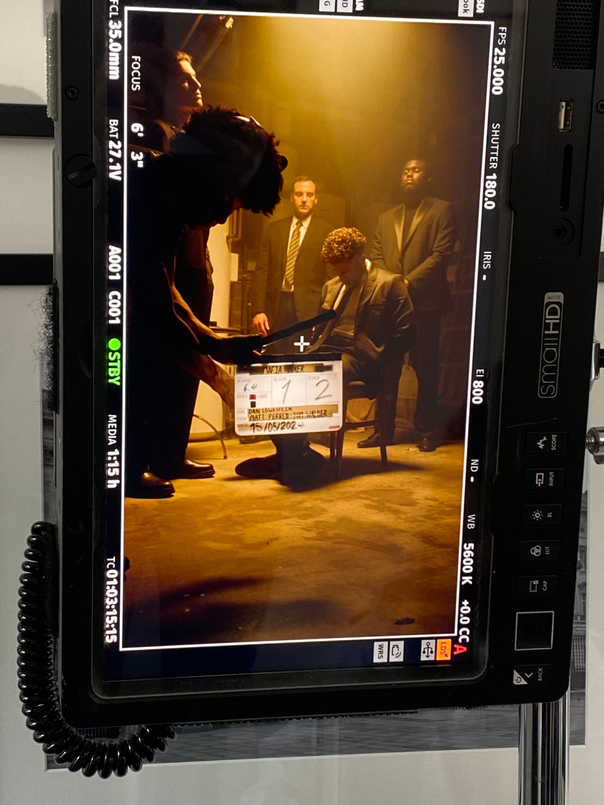 Behind the scenes - on-set monitor showing clapperboard with Tristan Alexander and cast in suits