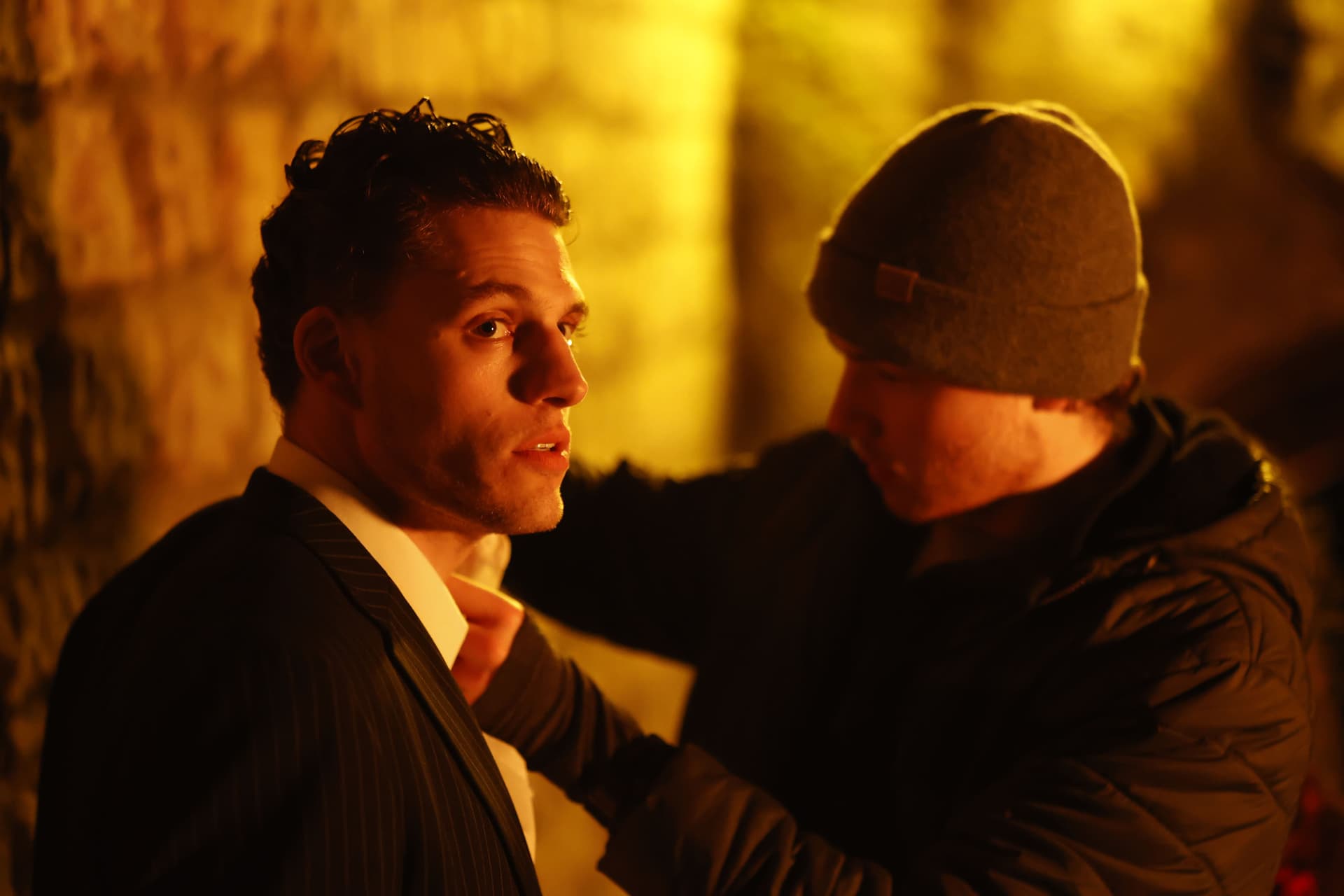 Tristan Alexander in a pinstripe suit in a tense confrontation scene with dramatic amber lighting