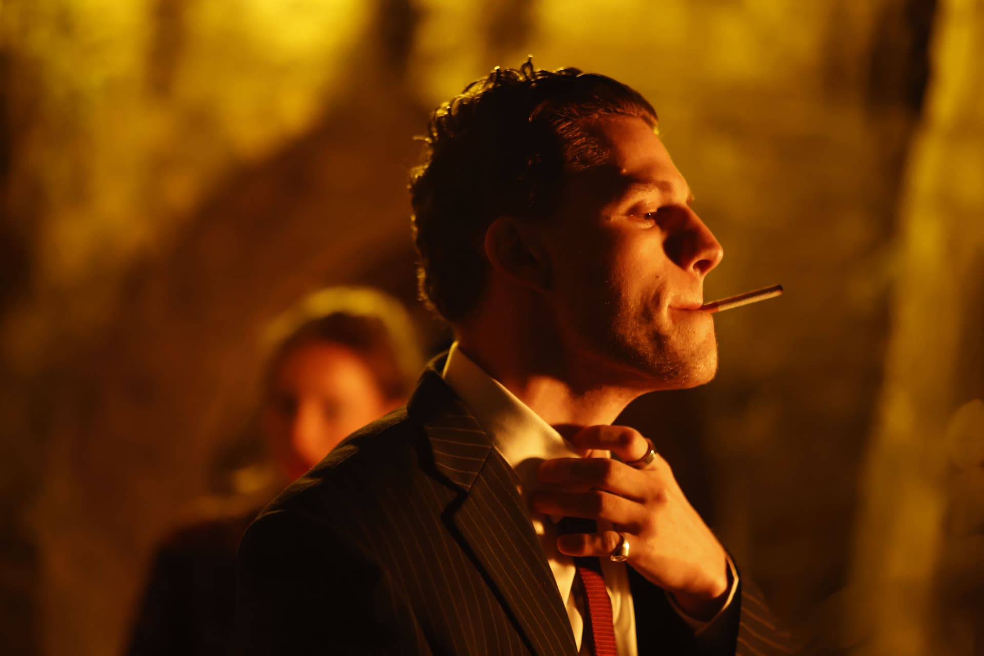Tristan Alexander smoking in profile wearing a pinstripe suit with dramatic amber lighting