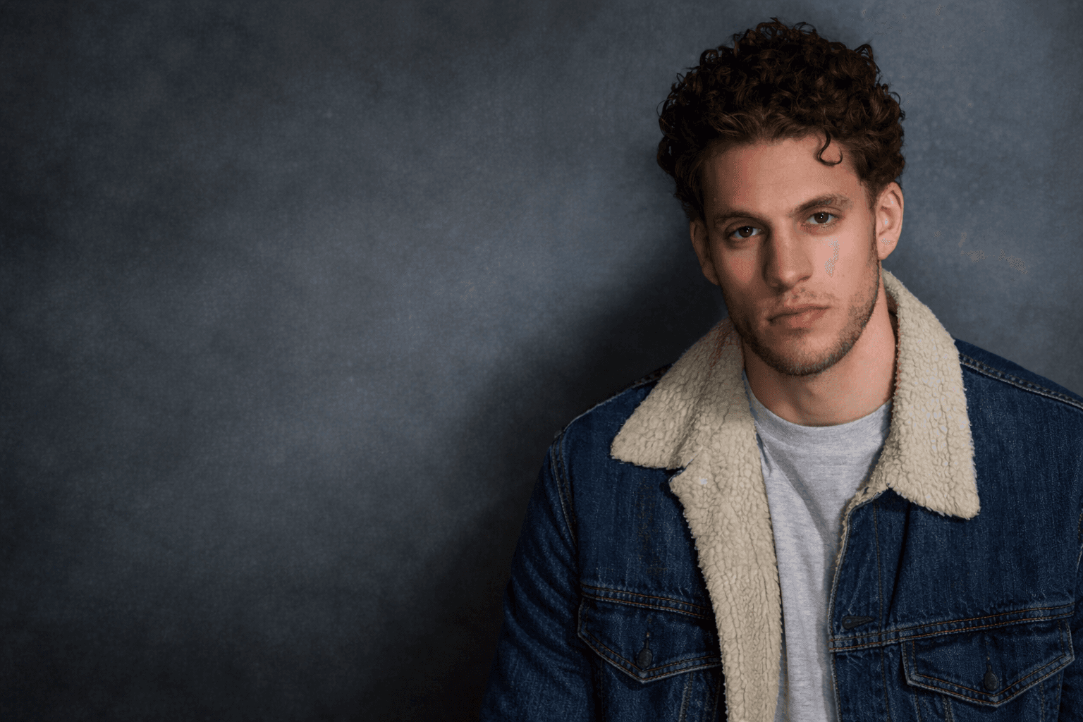 Tristan Alexander - headshot portrait in denim jacket against dark backdrop