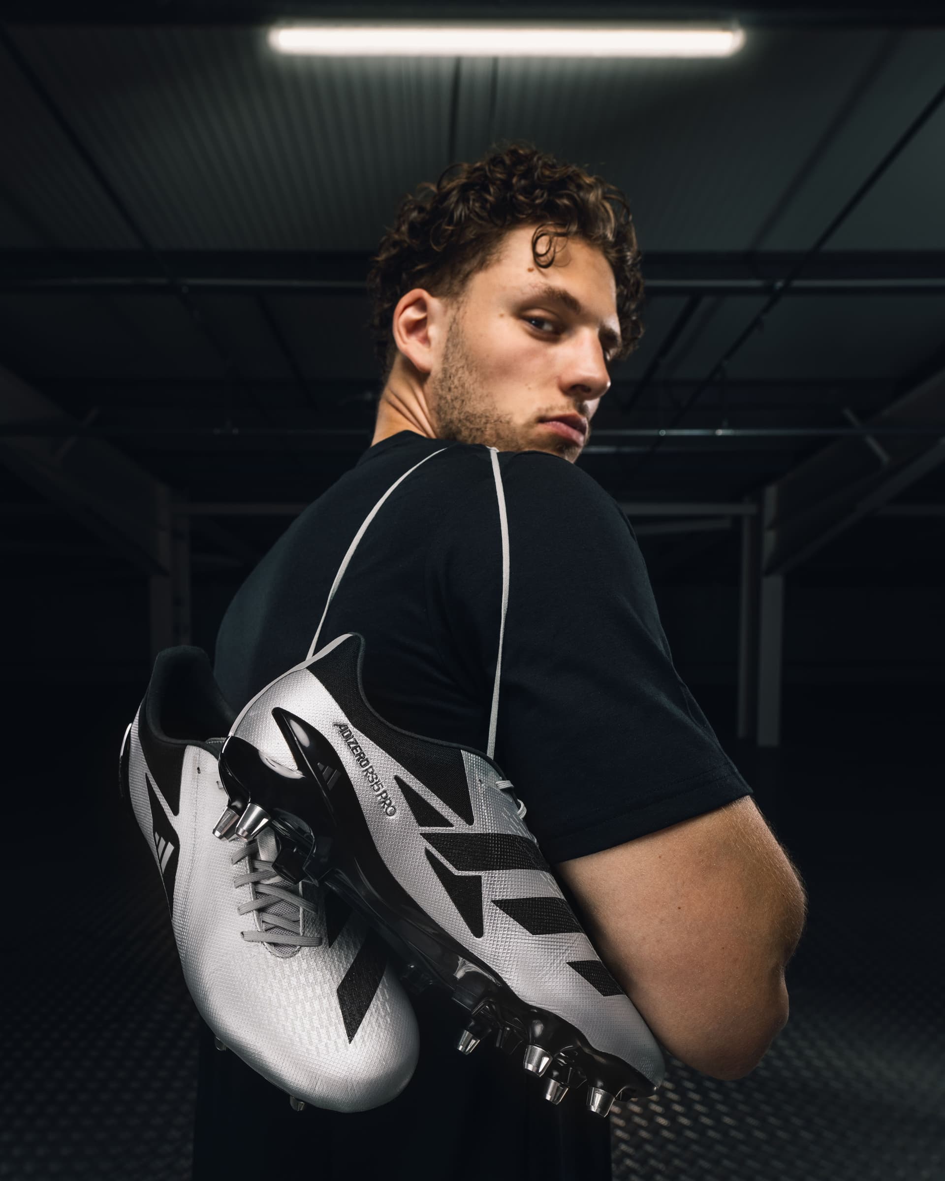 Tristan Alexander looking over his shoulder holding Adidas Adizero boots in a dark industrial setting