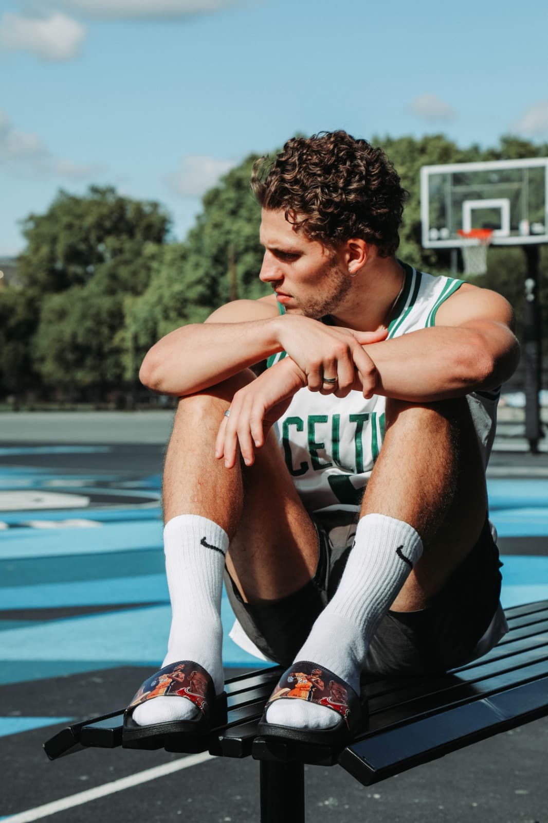 Tristan Alexander in a Celtics jersey sitting on a bench at an outdoor basketball court
