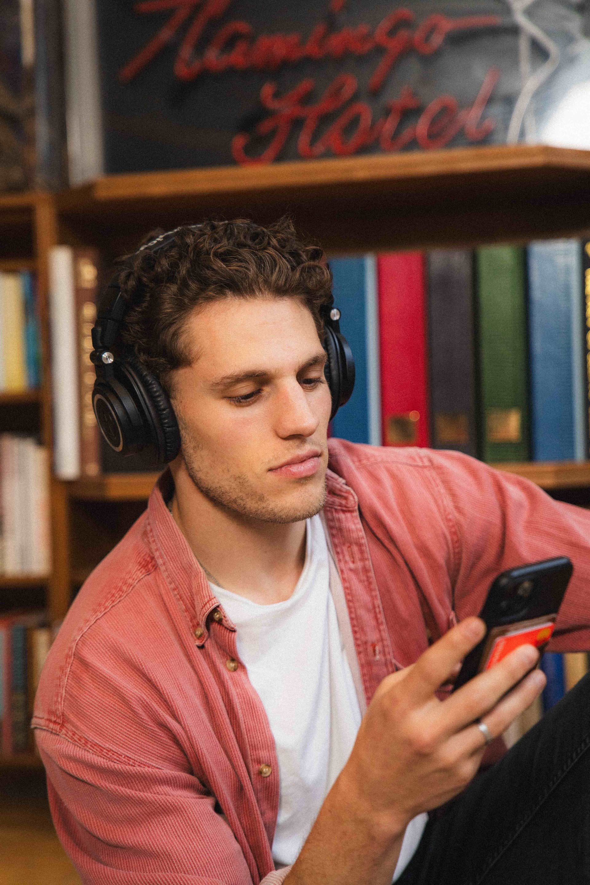 Tristan Alexander wearing Audio-Technica headphones and pink corduroy jacket browsing his phone