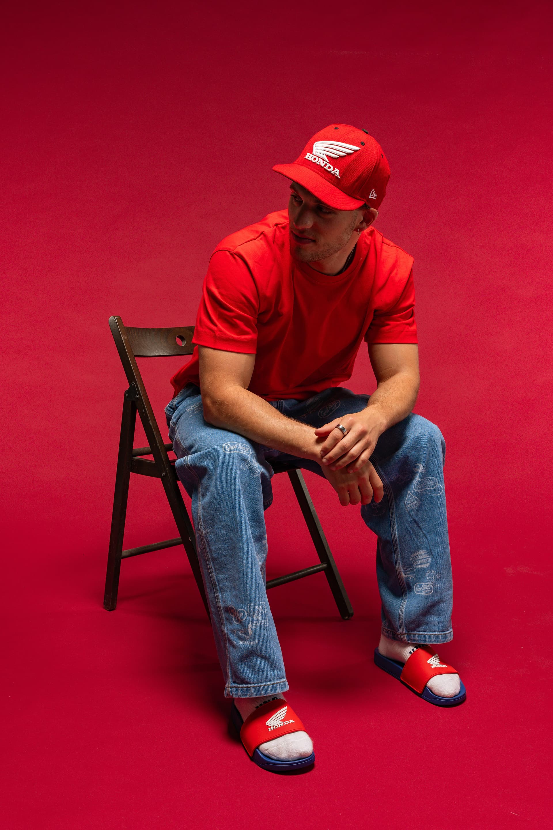 Tristan Alexander seated on a folding chair wearing Honda cap and red tee against a vivid red backdrop